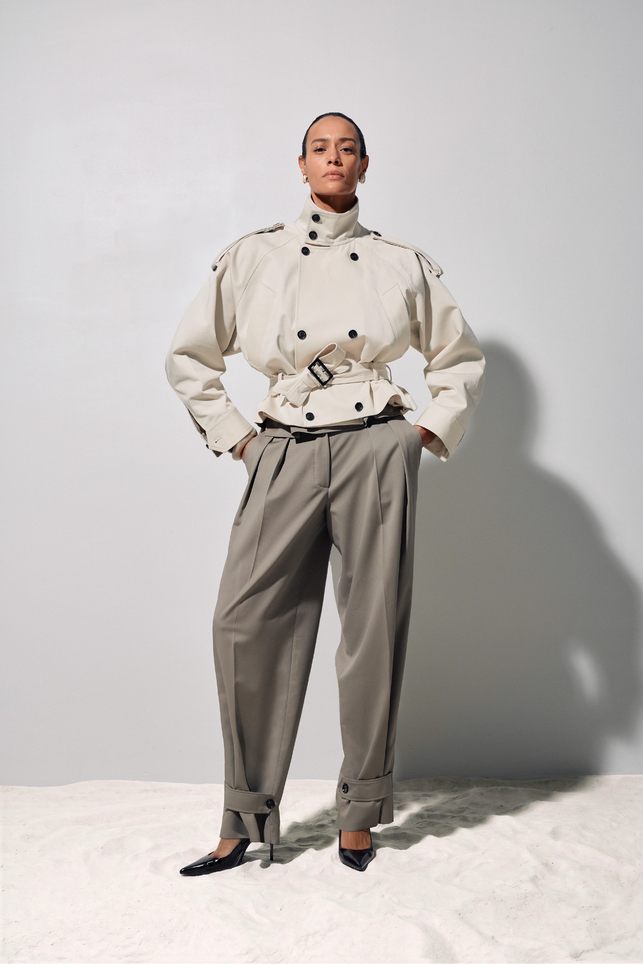 Person wearing a beige outfit with a high collar and wide-leg pants on a white background