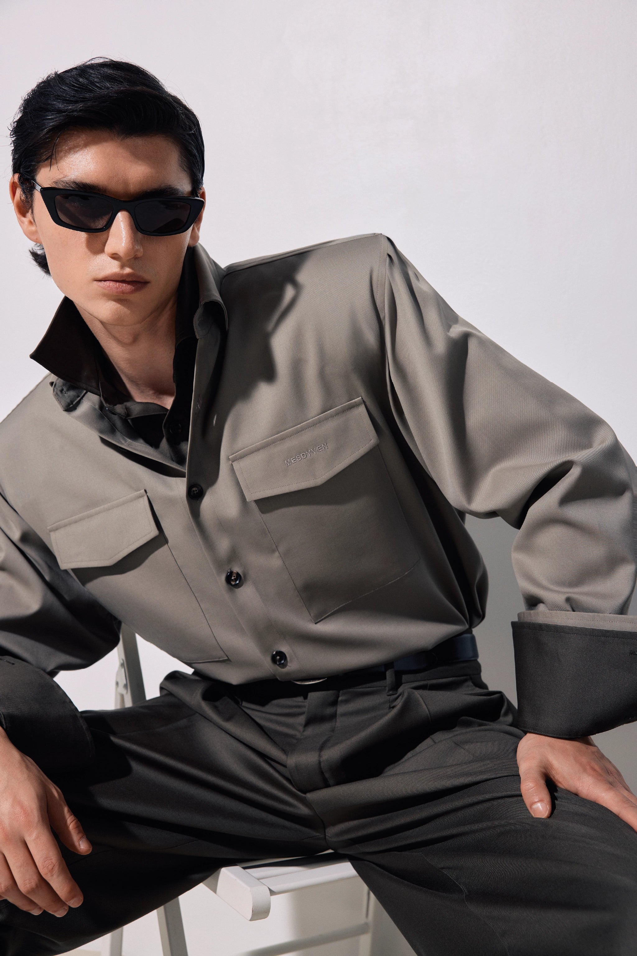 Person wearing a gray MESDYVEN shirt and black pants with sunglasses on a white background